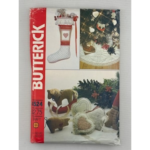 May include: A Butterick 4524 craft pattern envelope featuring illustrations of a Christmas stocking with a heart motif, a small stuffed horse on a red rocker, a pig, and several heart-shaped ornaments displayed near evergreen branches.