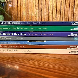 May include: A stack of seven hardcover books with colorful spines, including titles like Julie of the Wolves, Treasure Island, The House of Dies Drear, The Pigman, The Summer of the Swans, The Slave Dancer, and Across Five Aprils, all published by Glencoe McGraw-Hill.