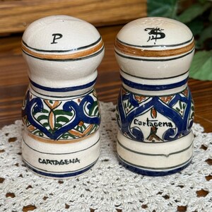 May include: Two ceramic salt and pepper shakers with a cream-colored crackle glaze finish. Each shaker features hand-painted blue, green, and orange floral patterns, with the word Cartagena and the letters P and S clearly marked on the surfaces.