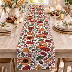 Può includere: Un lungo runner da tavola rettangolare caratterizzato da un motivo autunnale ripetuto con zucche arancioni, girasoli gialli, bacche rosse, ghiande marroni e foglie autunnali multicolori su sfondo bianco, con cuciture trapuntate visibili.