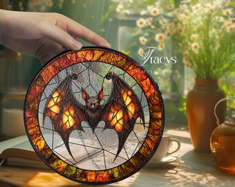 May include: Round stained glass art piece featuring a bat with outstretched wings. The bat is dark brown with orange and yellow accents. The border is a mosaic of orange, red, and yellow glass. The text "Tracys CraftHub" is visible.