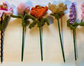 Puede incluir: Una colección de seis flores de ganchillo hechas a mano en varios colores. Las flores incluyen flores rosas, naranjas, amarillas y moradas con tallos y hojas verdes. Algunos tallos están decorados con alambre rojo y dorado.