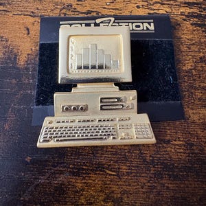 May include: A gold-toned metal lapel pin shaped like a vintage desktop computer. The monitor displays a bar graph with numbers 1 through 4 on the side. The base features a keyboard and a computer tower with visible drive slots and buttons.