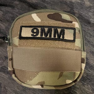 May include: A camouflage-patterned pouch with a black zipper and a black patch that reads "9MM".