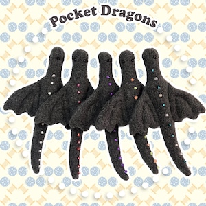 May include: Five dark gray felt dragon figures arranged in a row, each featuring small black bead eyes and a line of colorful, sparkling rhinestones running down the chest and tail. The text Pocket Dragons is arched above the figures.