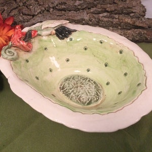 Puede incluir: Un bol de cerámica verde y blanco con un diseño floral. El bol tiene un borde festoneado y una superficie texturizada. El bol es perfecto para servir fruta, aperitivos u otros artículos pequeños.