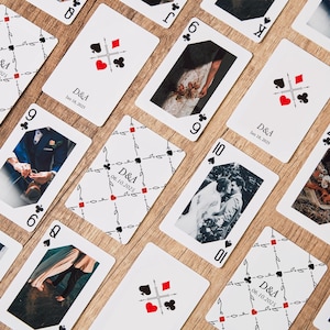 May include: A collection of playing cards with wedding photos and personalized details. The cards feature images of a couple, along with the initials "D&A" and a date. The cards are arranged on a wooden surface.