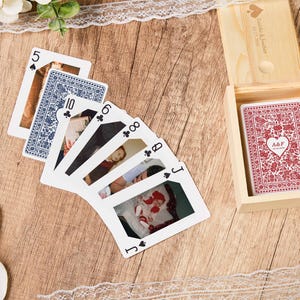 May include: A deck of custom playing cards featuring personal photographs on the faces and a red floral pattern with a heart icon on the back, stored in a light-coloured wooden box with a sliding lid engraved with a heart and text.