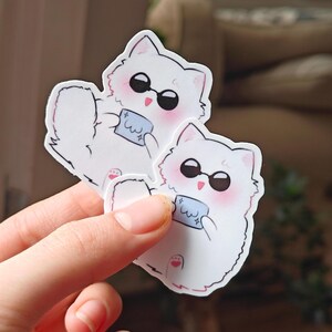 Jujutsu Kaisen Gojo cat sticker featuring a cute white fluffy cat wearing black sunglasses and holding a tiny cloth. This kawaii anime vinyl sticker is great for decorating journals, laptops, tumblers, phone cases, and water bottles!