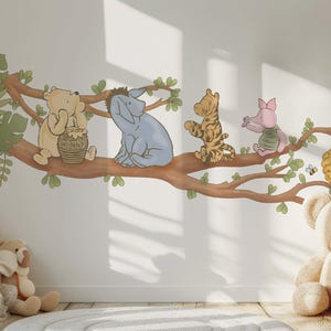 Op de afbeelding: Een Winnie de Poeh-muursticker met Winnie de Poeh, Biggetje, Eeyore en Teigetje die op een tak zitten. De sticker is perfect voor een kinderkamer of babykamer.