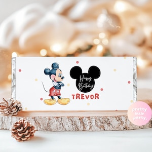 May include: A white candy bar wrapper featuring a watercolor illustration of Mickey Mouse. The wrapper includes the text "Happy Birthday TREVOR" and a black Mickey Mouse silhouette. Pink and yellow polka dots decorate the background.