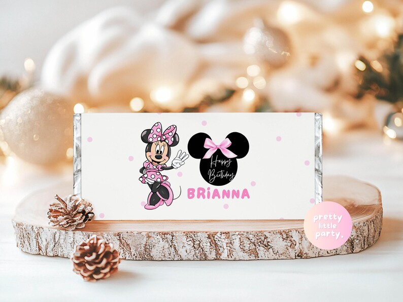 Puede incluir: Envoltorio blanco de barra de caramelo con Minnie Mouse en rosa y negro. El envoltorio tiene el texto "Happy Birthday Brianna" y lunares rosas. Se muestra sobre una rodaja de madera.