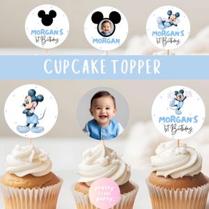 Puede incluir: Adornos para cupcakes con dise&ntilde;os de Mickey Mouse y una foto de beb&eacute;. Los adornos redondos tienen un esquema de color azul y blanco, algunos con el texto "Morgan's 1st Birthday". La imagen tambi&eacute;n incluye cupcakes con glaseado blanco.