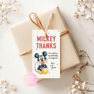 May include: A gift wrapped in beige paper and tied with twine, featuring a Mickey Mouse themed tag. The tag reads "MICKEY THANKS" with the text "for making my birthday so magical!" and "love, Trevor". The tag has a cartoon image of Mickey Mouse.