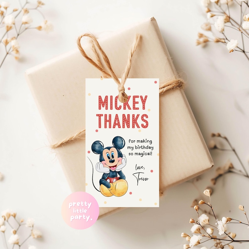May include: A gift wrapped in beige paper and tied with twine, featuring a Mickey Mouse themed tag. The tag reads "MICKEY THANKS" with the text "for making my birthday so magical!" and "love, Trevor". The tag has a cartoon image of Mickey Mouse.
