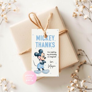 Puede incluir: Una etiqueta de regalo con una ilustraci&oacute;n de Mickey Mouse y la frase azul "MICKEY THANKS". La etiqueta dice "for making my birthday so magical! love, Morgan." La etiqueta est&aacute; atada a un regalo envuelto con hilo.