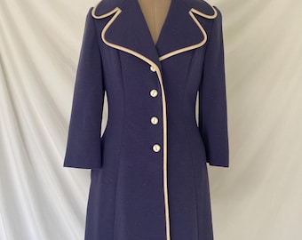 May include: A navy blue coat with a white trim around the collar, cuffs, and down the front. The coat has a button closure and a fitted silhouette.