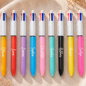 May include: Nine colorful multi-color pens with names printed on them. The pens have white barrels and are in various colors, including yellow, red, purple, blue, pink, teal, black, and yellow. Each pen has a different name printed on it.