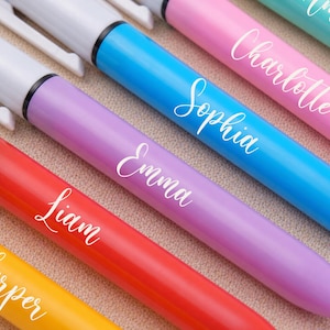 May include: A close-up of several colorful markers, each with a different name in white script. The markers are in shades of yellow, red, purple, blue, pink, and teal. The names include Harper, Liam, Emma, Sophia, Charlotte, and Amelia.
