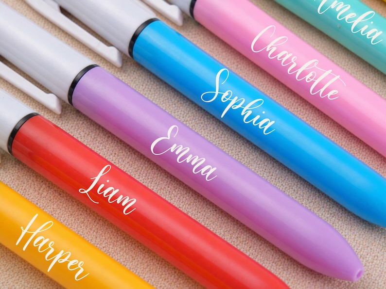 May include: A close-up of several colorful markers, each with a different name in white script. The markers are in shades of yellow, red, purple, blue, pink, and teal. The names include Harper, Liam, Emma, Sophia, Charlotte, and Amelia.