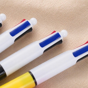 May include: Close-up of several multi-color pens. Each pen has a white barrel with a different colored button on top. The pens have black, red, blue, and yellow accents. The pens are arranged diagonally on a beige surface.
