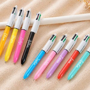May include: A collection of colorful multi-color pens with white barrels. Each pen has a different colored barrel and the names Olivia, Harper, Evelyn, Arthur, Sophia, Charlotte, Emma, Liam, and Amelia are printed on the pens.