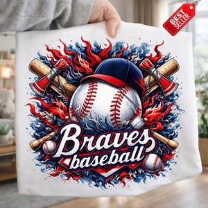 Peut inclure: Design graphique sur le thème du baseball, avec une balle, une casquette et des tomahawks croisés. Le design comprend le texte "Braves baseball" dans une police stylisée, avec des accents rouges, blancs et bleus. Une étiquette "Meilleur vendeur" est visible.