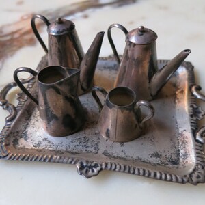 May include: A silver tea set with a teapot, creamer, and sugar bowl on a silver tray. The set is made of metal and has a vintage look.