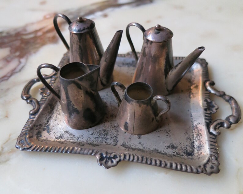 May include: A silver tea set with a teapot, creamer, and sugar bowl on a silver tray. The set is made of metal and has a vintage look.