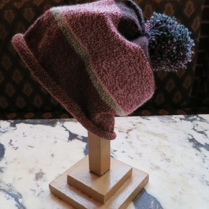 May include: A striped knit hat with a large pom-pom on top. The hat is displayed on a wooden stand.