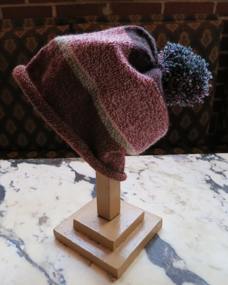 May include: A striped knit hat with a large pom-pom on top. The hat is displayed on a wooden stand.