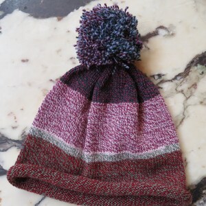 May include: A striped knit beanie with a pom pom on top. The beanie is red, green, gray, and pink.