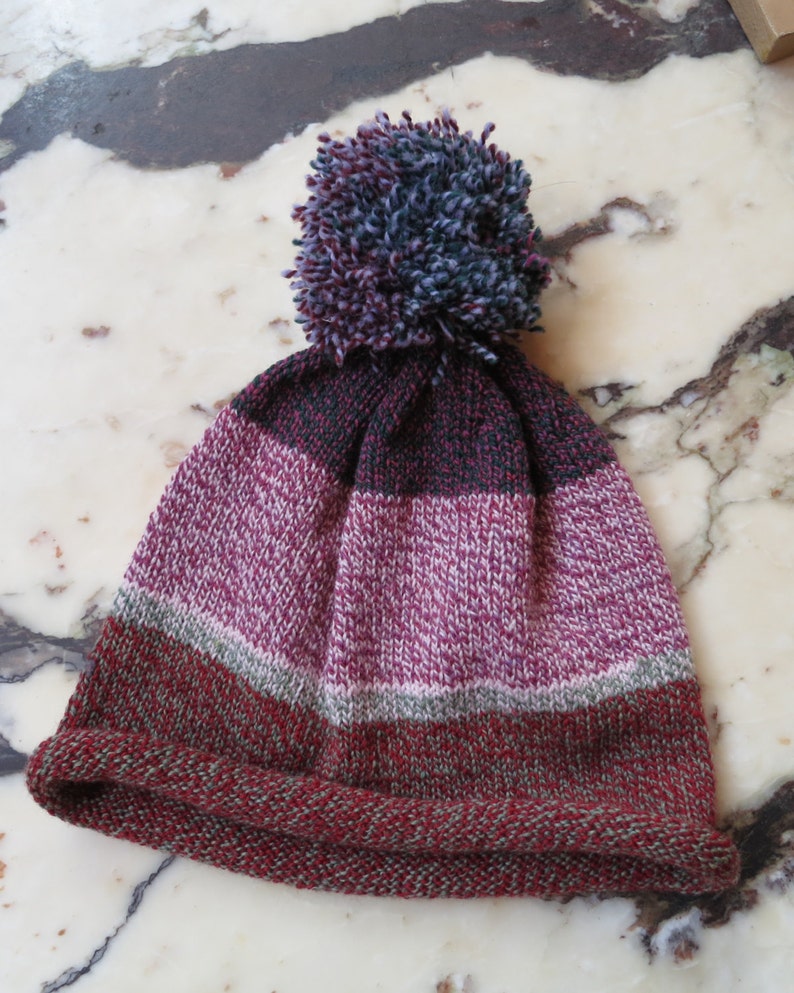 May include: A striped knit beanie with a pom pom on top. The beanie is red, green, gray, and pink.