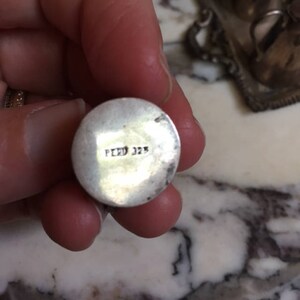 May include: Close-up of the bottom of a silver pendant with the inscription "Peru 325" on the back.