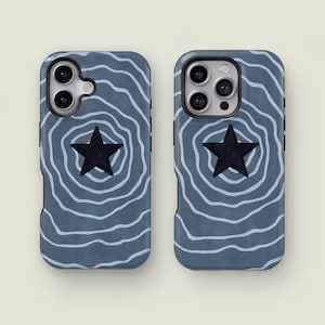 Op de afbeelding: Twee telefoonhoesjes met een blauwgrijze achtergrond en een wit, golvend patroon. Elke hoes heeft een zwarte ster in het midden. De hoesjes zijn ontworpen voor een smartphone en bieden bescherming en een unieke uitstraling.