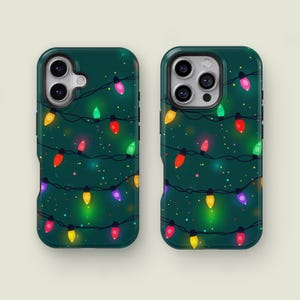 May include: Two phone cases with a dark green background and a pattern of colourful Christmas lights. The lights are yellow, red, green, pink, and purple. The cases have a glossy finish.