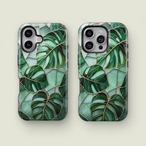 May include: Two phone cases with a stained glass design featuring large green monstera leaves with gold outlines on a light green background. The cases have a glossy finish and are designed to fit a smartphone.