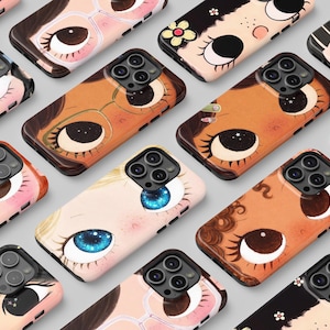 Op de afbeelding: Een verzameling telefoonhoesjes met illustraties van gestileerde gezichten met grote ogen, wimpers en verschillende haarkleuren. Sommige hoesjes hebben brillen, bloemen of sterdetails. De hoesjes zijn in tinten roze, bruin en zwart.