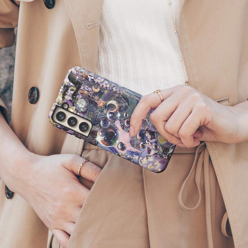 May include: A smartphone case with a colorful, artistic design featuring bubbles, stars, and celestial elements in shades of purple, blue, and gold. The case has a glossy finish and a camera cutout.