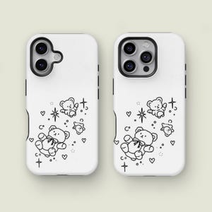 May include: Two white phone cases with a black and white teddy bear design. The cases feature a repeating pattern of teddy bears, hearts, stars, and crosses. The cases are for a smartphone.