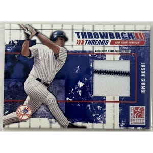 May include: A 2003 Donruss Elite Throwback Threads trading card featuring Jason Giambi in a pinstriped New York Yankees uniform swinging a bat. The card includes an embedded piece of an authentic game-worn white jersey with a navy blue stripe.