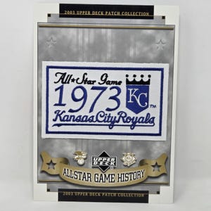 Könnte beinhalten: Eine gerahmte Karte der Upper Deck Patch Collection 2003. Die Karte zeigt einen Patch mit "All-Star Game 1973 Kansas City Royals" in Blau und Weiß. Die Karte hat auch ein goldenes Banner mit der Aufschrift "All-Star Game History".