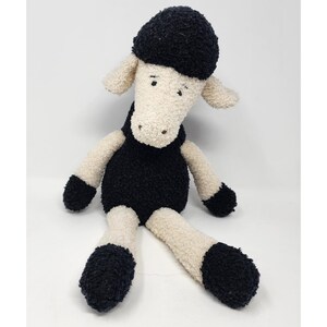 May include: A plush sheep toy with a black body, head, and feet, and cream-colored face, arms, and legs. The stuffed animal has a soft, textured appearance and is sitting upright. The sheep has small, embroidered eyes and a simple, friendly expression.