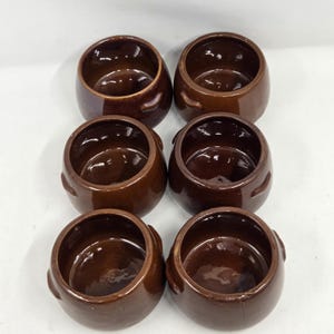 May include: A set of six matching dark brown ceramic pots arranged in two columns of three. Each pot features a rounded, bulbous body with a smooth, glossy glaze finish and two small, integrated side handles near the top rim of the vessel.
