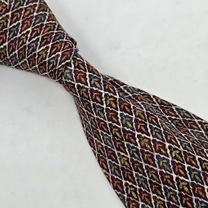 May include: A patterned necktie with a repeating leaf design in burgundy, navy, gold, and white. The tie is knotted, showcasing the intricate pattern and color variations. The tie is made of a smooth fabric.