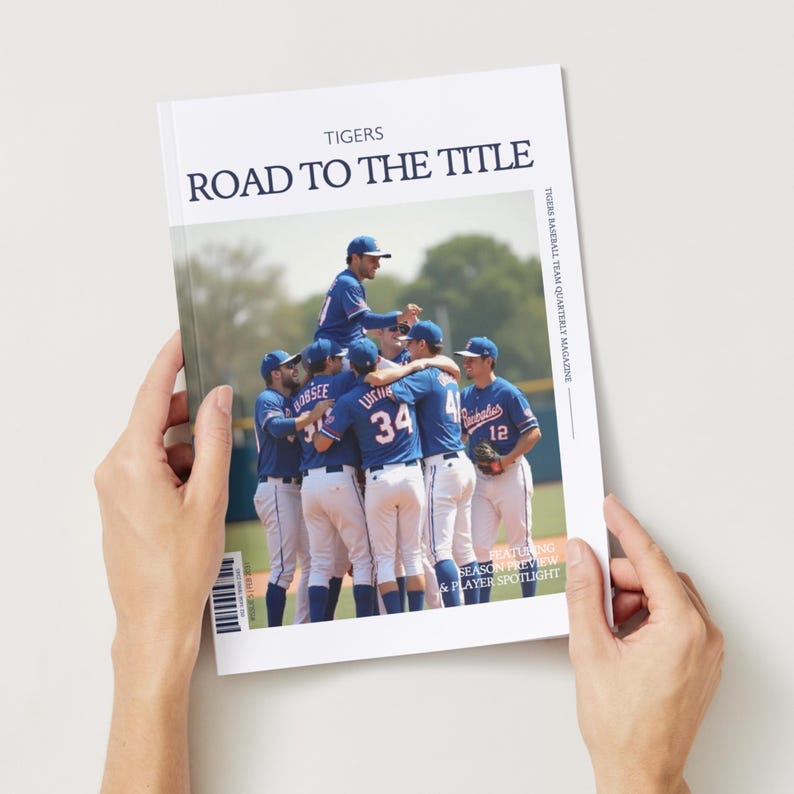 May include: A magazine cover with the title "ROAD TO THE TITLE" and the word "TIGERS" at the top. The cover features a team of baseball players in blue uniforms celebrating a victory. The magazine is held by hands.