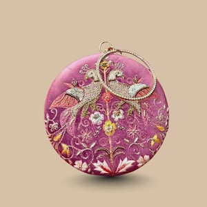 May include: A round, magenta clutch with an embroidered design featuring two birds and floral patterns. The clutch has a gold-colored handle and is embellished with beads and sequins. The overall design is intricate and detailed.