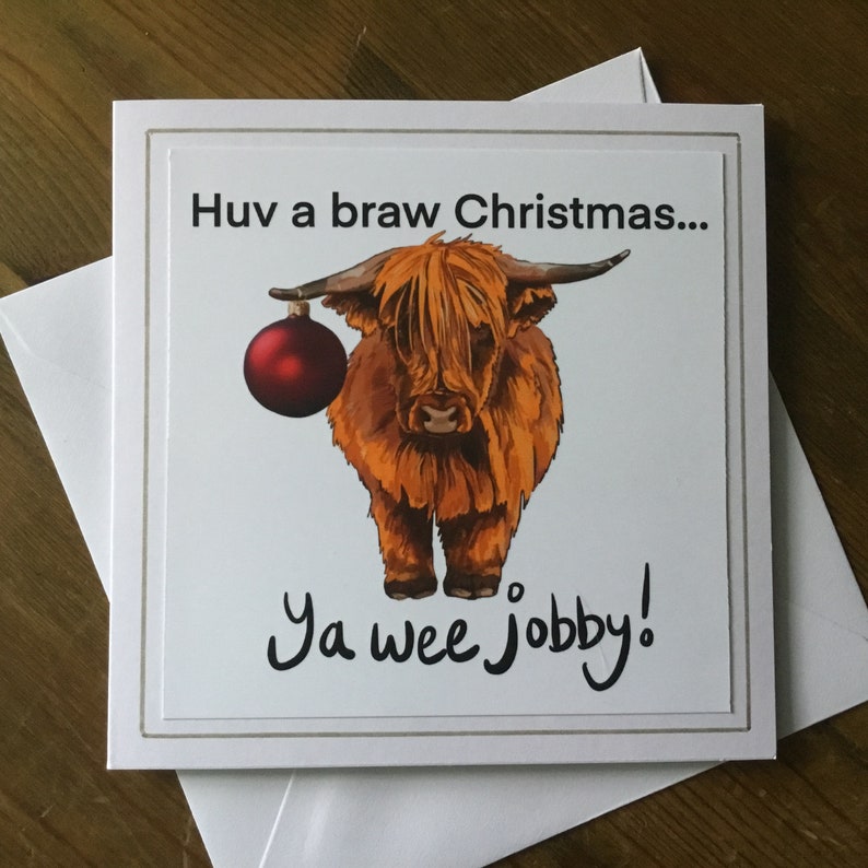 Square card with highland cow wearing a Christmas bauble.
