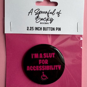 May include: A 5.7 cm circular button pin in black with hot pink text that reads I'M A SLUT FOR ACCESSIBILITY and a wheelchair symbol. The pin is packaged in a clear plastic sleeve attached to a white card labelled A Spoonful of Becky DESIGNS.
