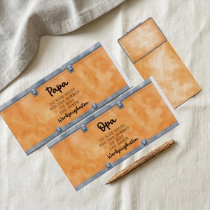 Pode incluir: Um conjunto de artigos de papelaria com um design em aquarela. O conjunto inclui dois cart&otilde;es com a palavra "Papa" e um com "Opa", um bloco de notas e uma caneta de madeira. Os cart&otilde;es t&ecirc;m um design de couro sint&eacute;tico com texto em alem&atilde;o.